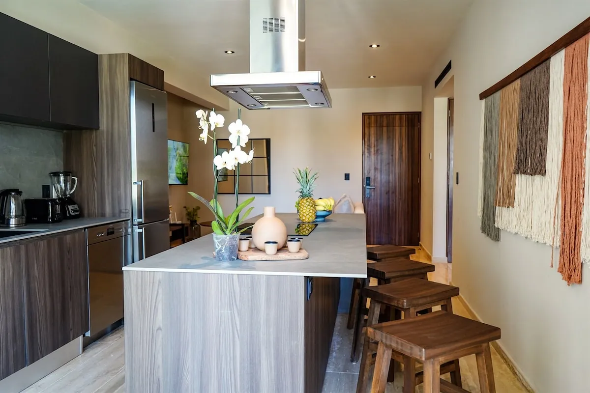 Cocina equipada con isla de mármol, orquídeas y tapiz artesanal mexicano en Hacienda Tuk