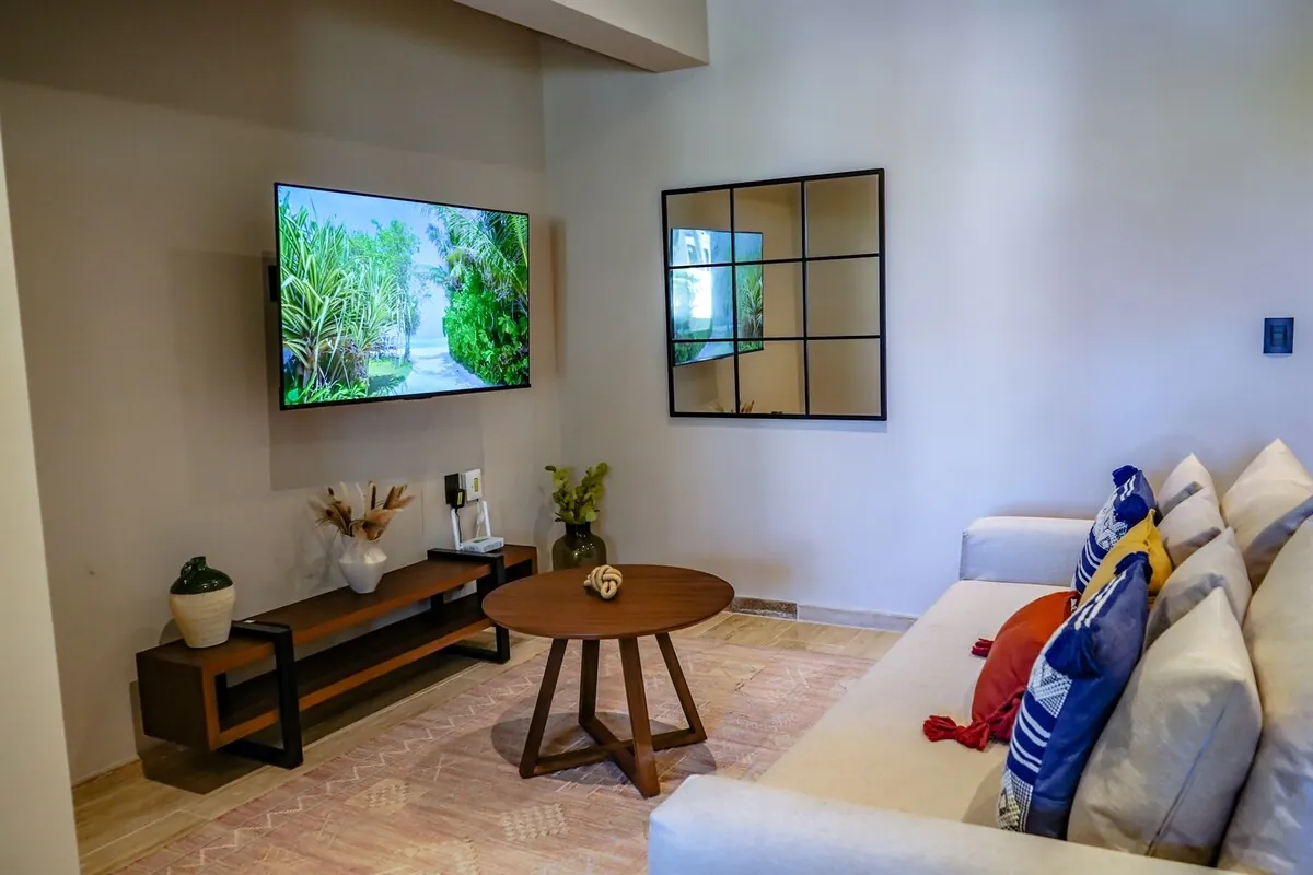Sala del departamento con sofá blanco, televisión y mesa redonda de madera