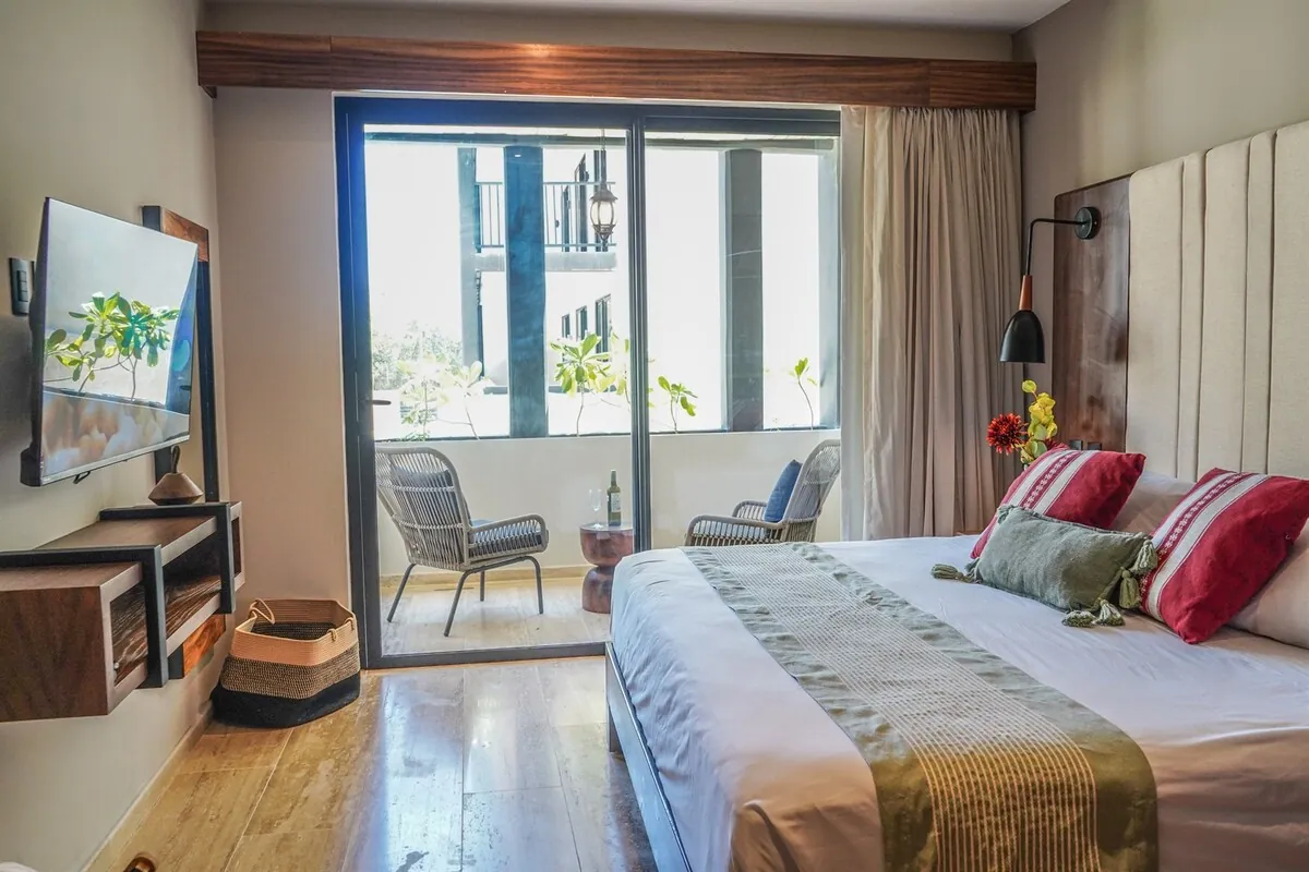 Recámara principal con ventanal al balcón privado y cama con cojines rojos