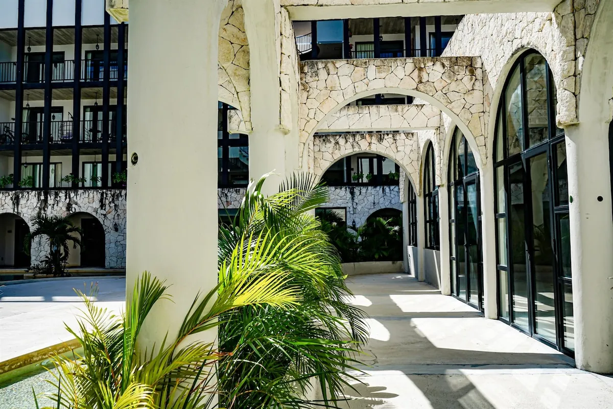 Corredor de arcos de piedra del conjunto Tuk Tulum con palmeras