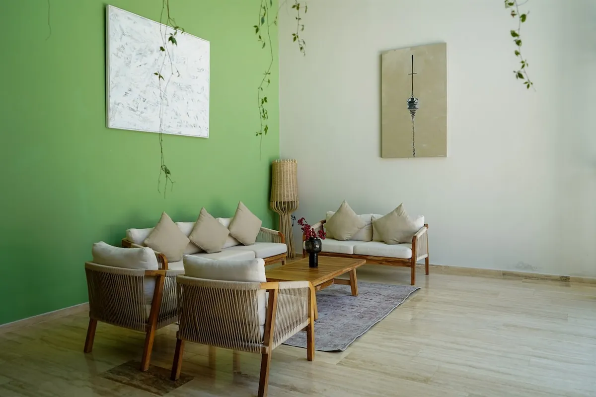 Sala de estar común con pared verde, sillones de mimbre y alfombra clara