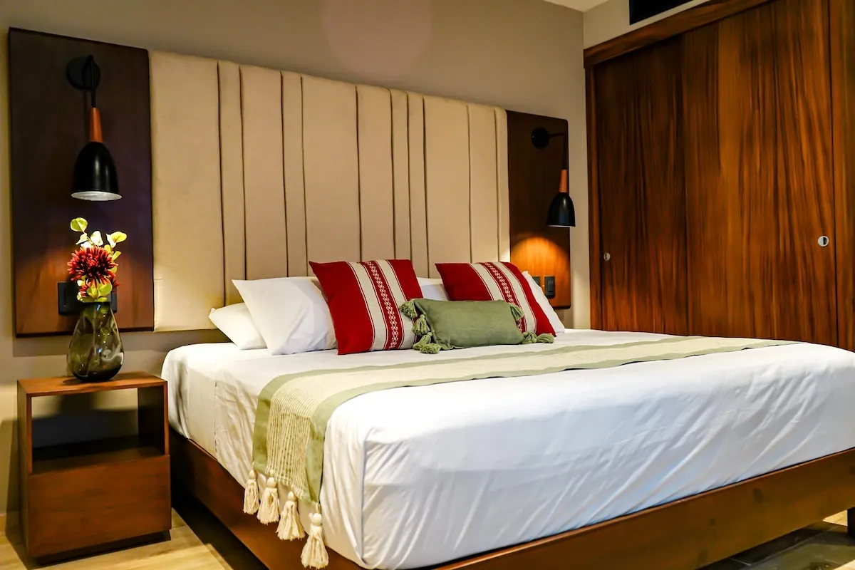 Recámara con cama king, flores frescas y buró de madera oscura