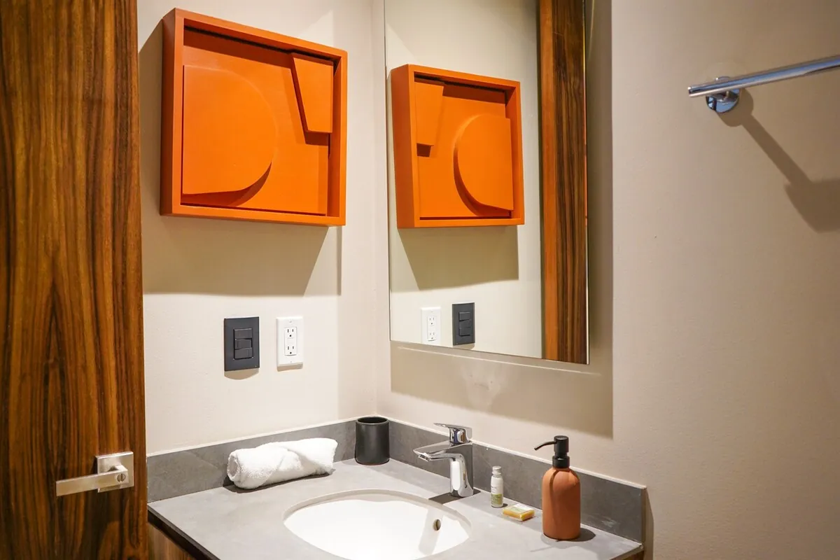 Baño con lavabo de piedra, cuadros naranjas y toallas dobladas